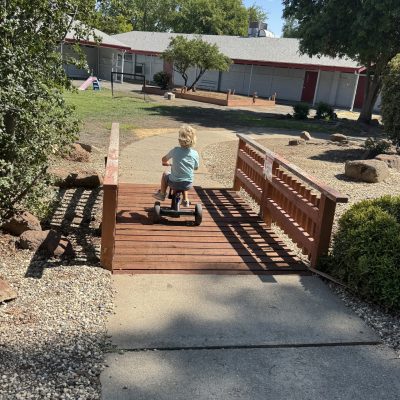 Image of a young child riding a tricycle across a wooden bridge